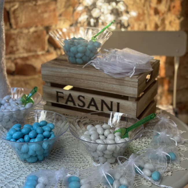 Tavolo sala eventi decorato con confetti azzurri per battesimo nella saletta per eventi di Fasani ad abbiategrasso con illuminazione intima e cassa di legno con marchio fasani